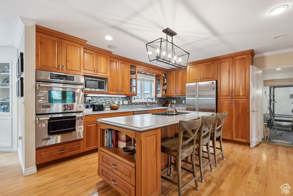 Kitchen with appliances with stainless steel finishes, brown cabinets, decorative backsplash, a center island, and a breakfast bar