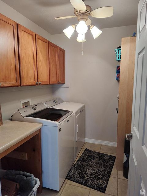 Washroom with cabinet space, washer and dryer, a ceiling fan, light tile patterned floors, and baseboards