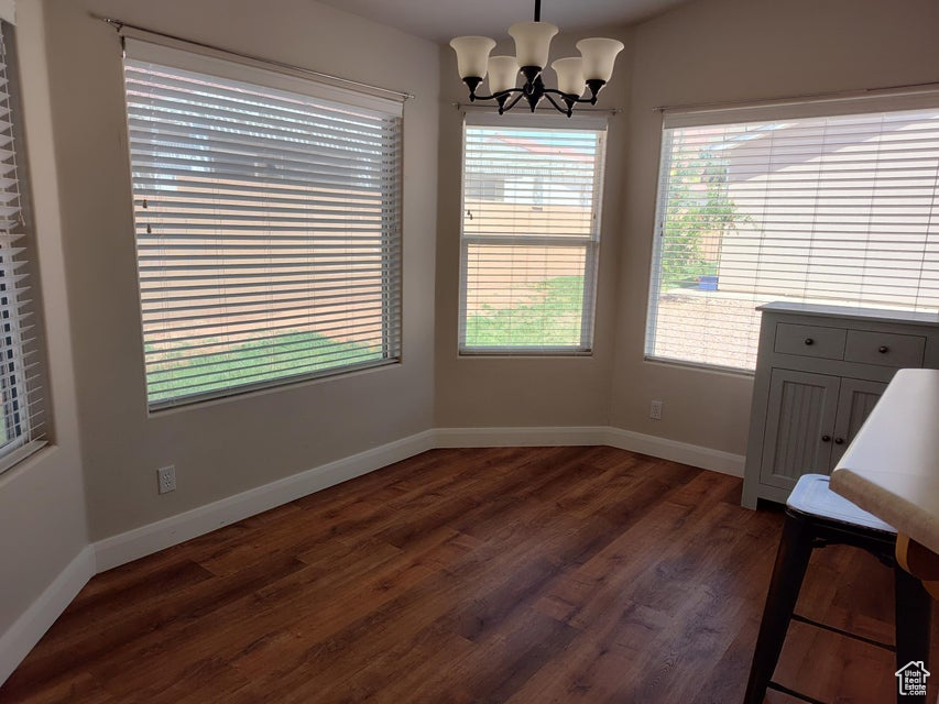 Unfurnished dining area featuring dark wood-type flooring, a chandelier, and baseboards