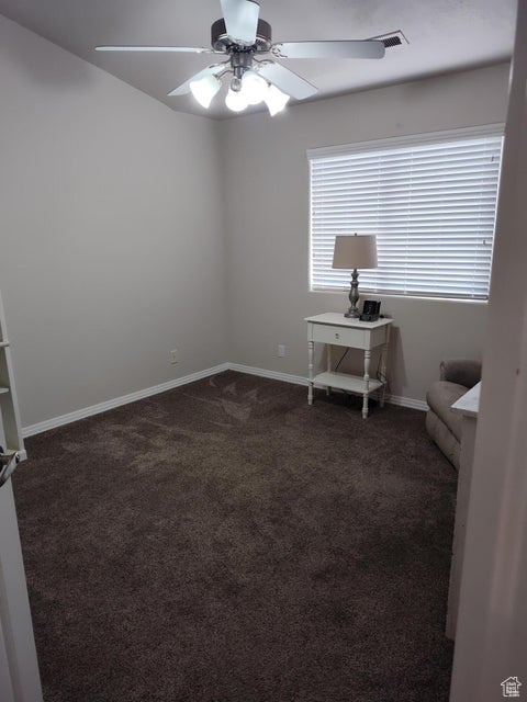 Unfurnished room featuring a ceiling fan, dark carpet, and baseboards