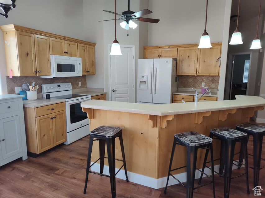 Kitchen with white appliances, decorative backsplash, a ceiling fan, dark wood finished floors, and a breakfast bar area