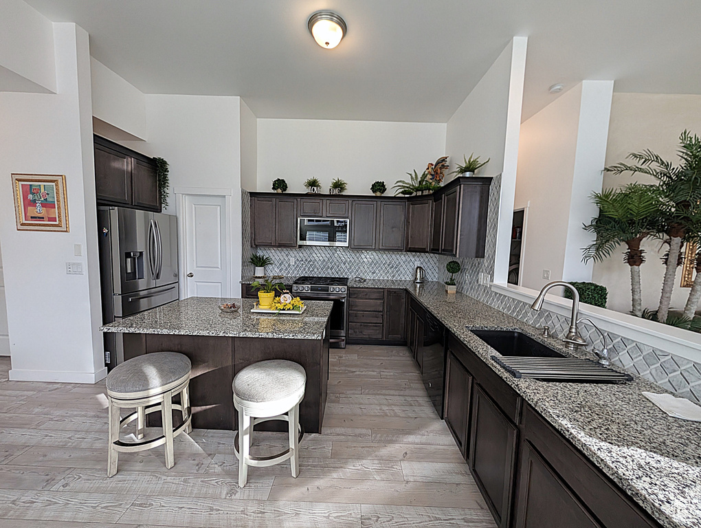 Kitchen featuring stainless steel appliances, a sink, a kitchen bar, and light stone countertops