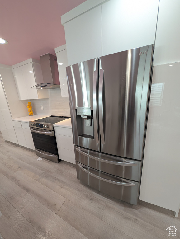 Kitchen featuring stainless steel appliances, wall chimney exhaust hood, modern cabinets, white cabinetry, and recessed lighting