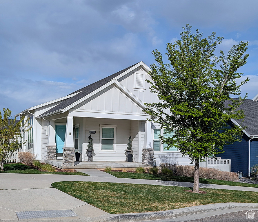 View of front of home with board and batten siding, a porch, a front yard, and stone siding