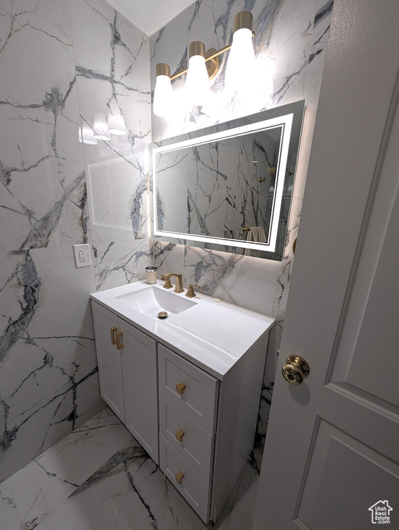 Bathroom with vanity, marble tiled flooring, and stone wall