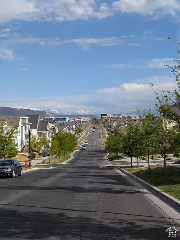 View of asphalt street featuring curbs, a mountain view, a residential view, and street lighting