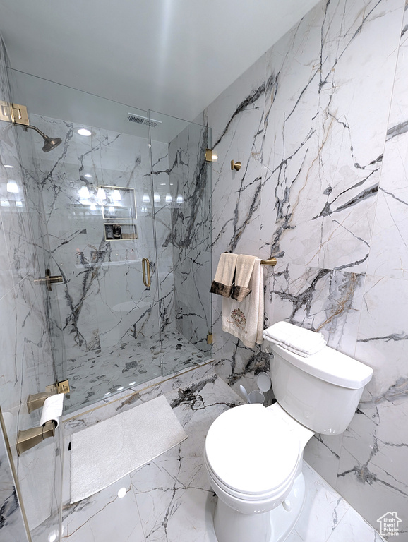 Full bath featuring marble tiled flooring, toilet, a marble finish shower, and stone wall