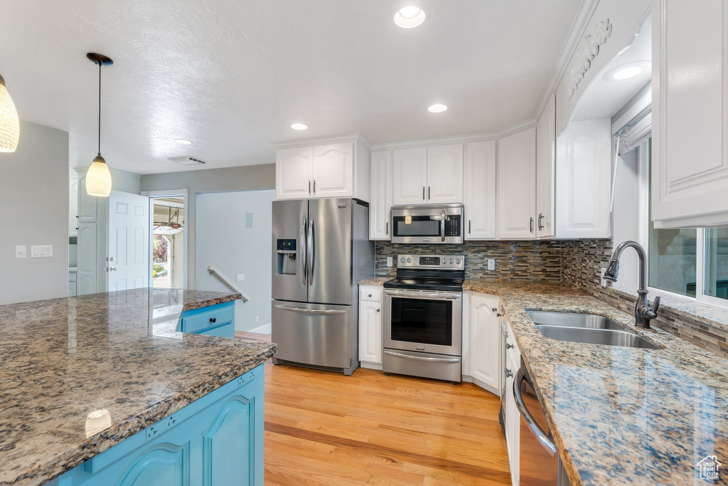 Kitchen with appliances with stainless steel finishes, a sink, light wood-style floors, white cabinetry, and decorative backsplash