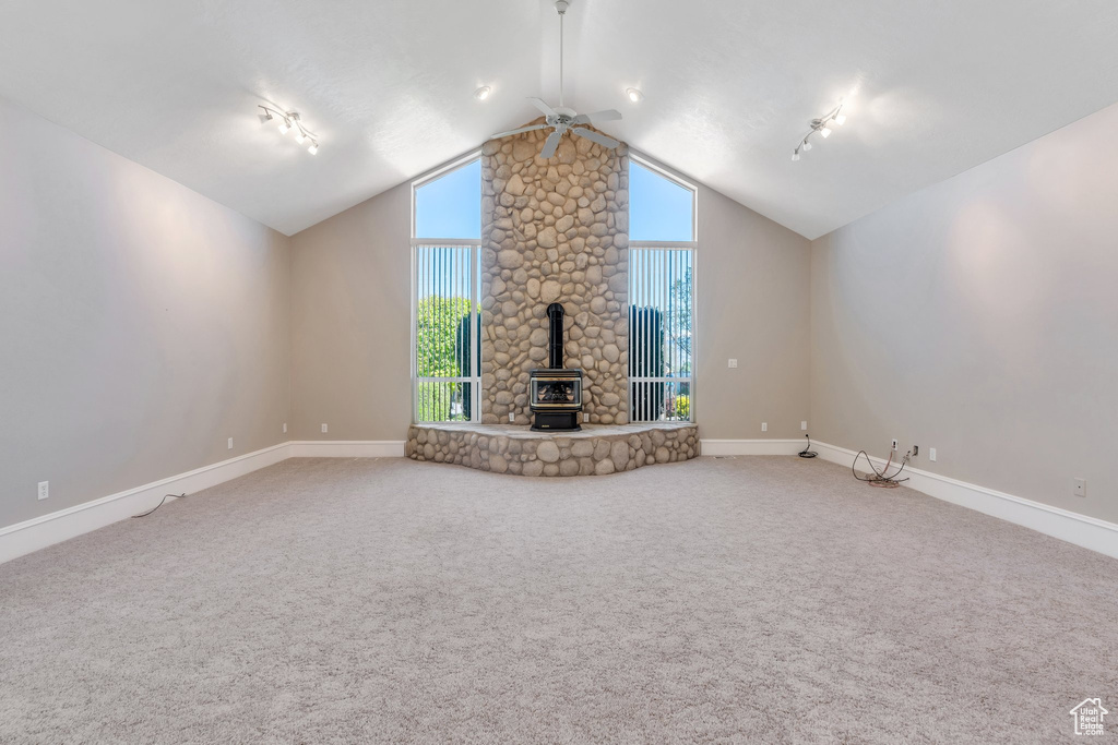 Unfurnished living room featuring a ceiling fan, a wood stove, vaulted ceiling, baseboards, and carpet