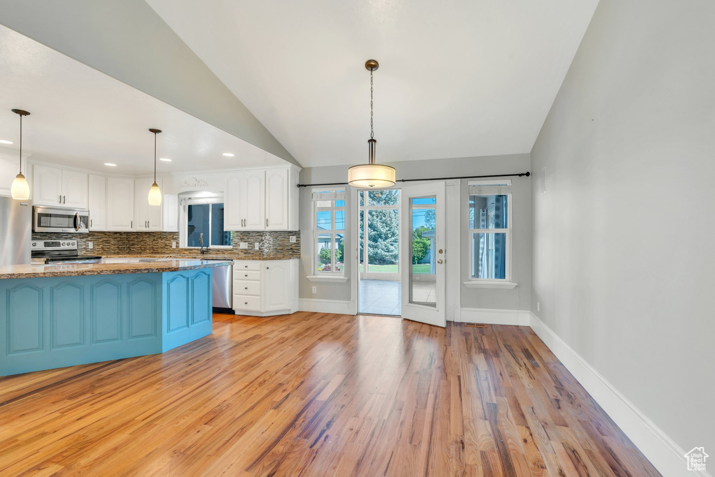 Kitchen with appliances with stainless steel finishes, white cabinets, light wood finished floors, backsplash, and vaulted ceiling