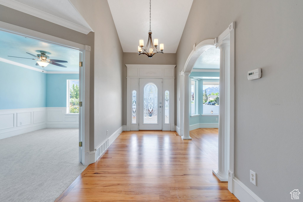 Foyer featuring decorative columns, plenty of natural light, arched walkways, vaulted ceiling, and light wood finished floors