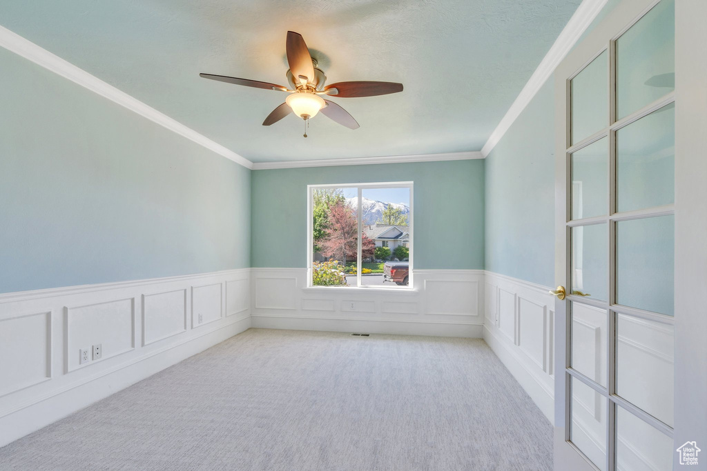 Unfurnished room with carpet flooring, a ceiling fan, ornamental molding, and wainscoting