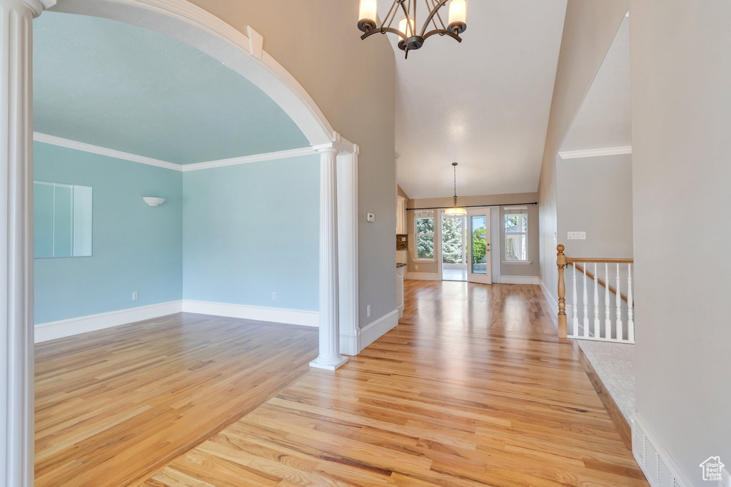 Foyer entrance with ornate columns, arched walkways, a high ceiling, light wood-style flooring, and a chandelier