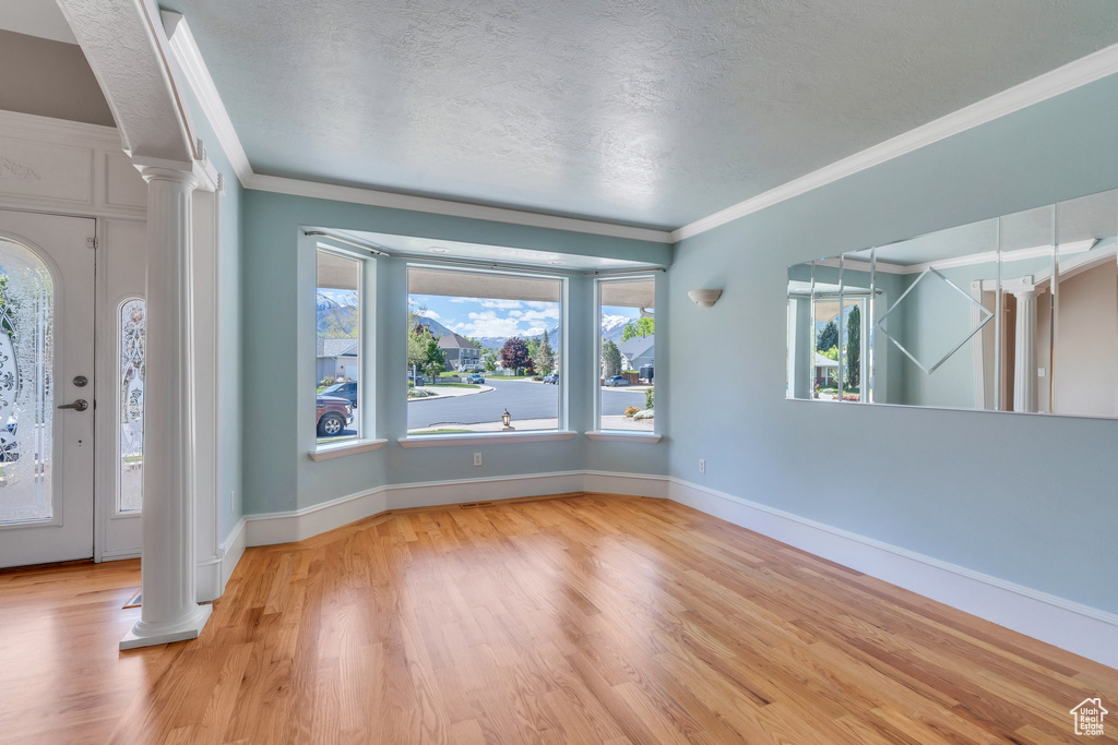 Foyer entrance featuring decorative columns, wood finished floors, ornamental molding, a textured ceiling, and baseboards