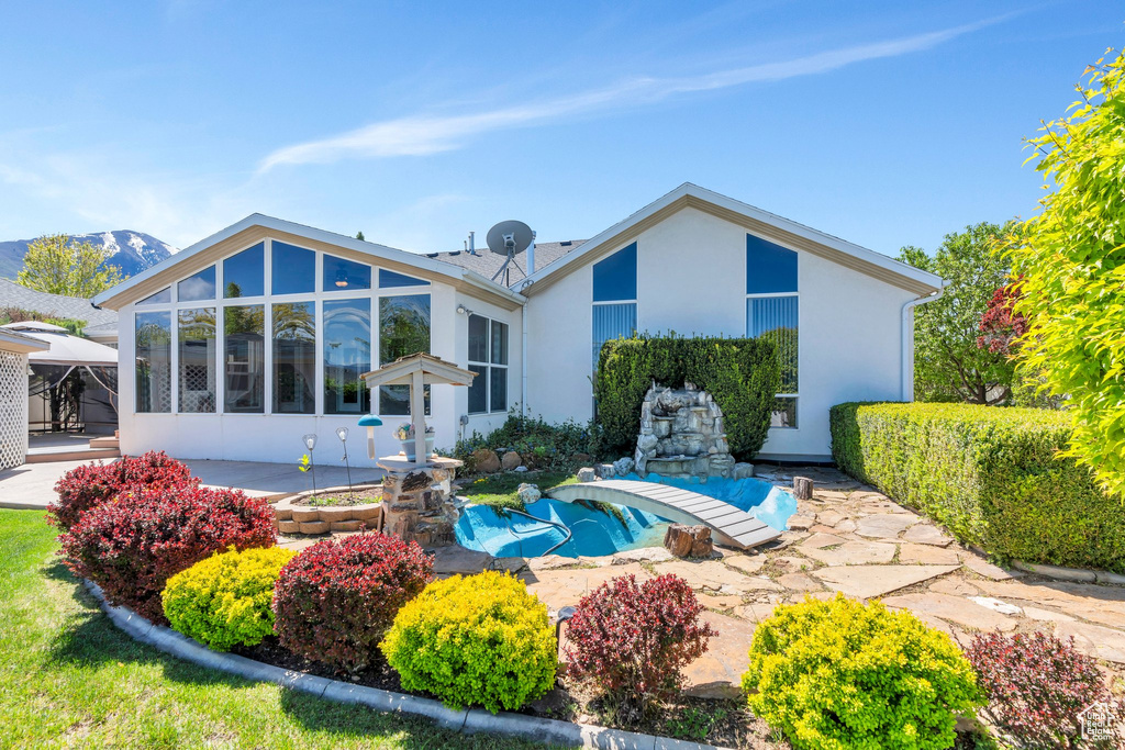 Rear view of house featuring stucco siding, a sunroom, and a patio