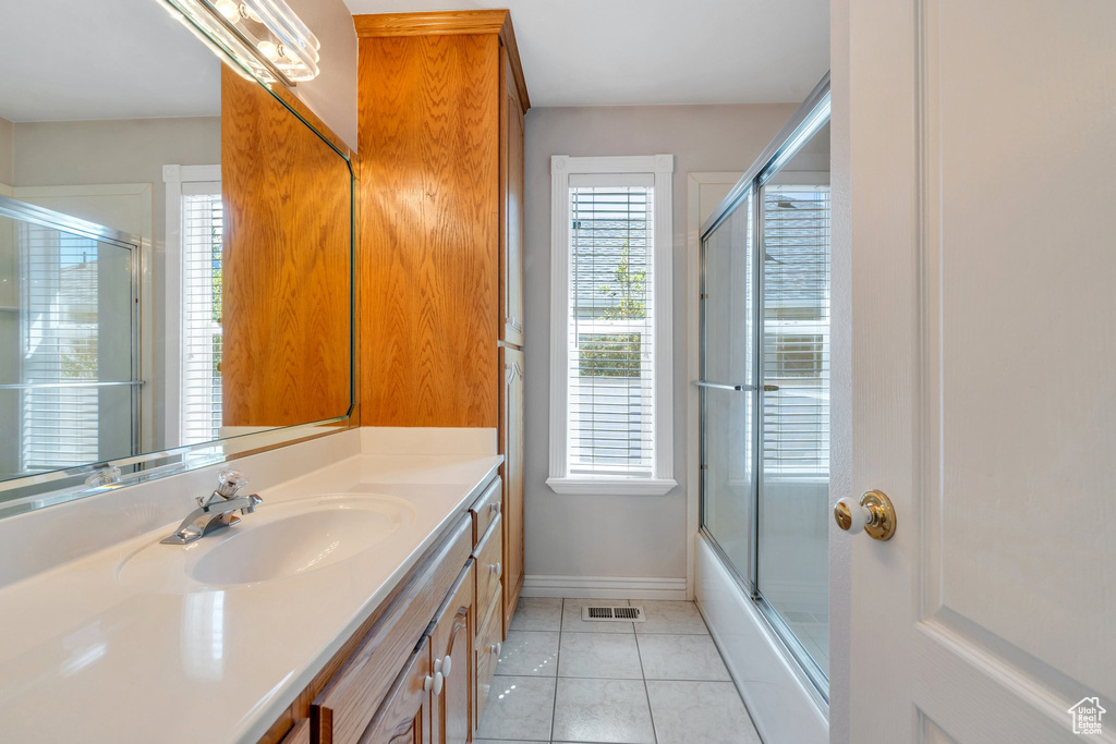 Bathroom featuring vanity, tile patterned flooring, baseboards, and bath / shower combo with glass door