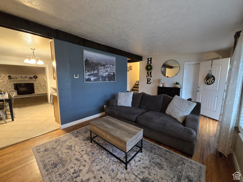 Living area with stairs, wood finished floors, a textured ceiling, a chandelier, and a fireplace with raised hearth