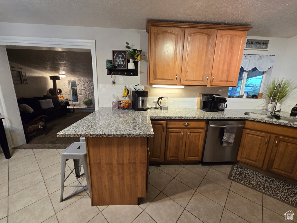 Kitchen featuring stainless steel dishwasher, light stone counters, backsplash, a breakfast bar area, and a peninsula
