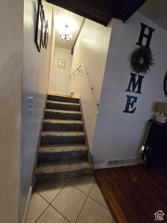 Staircase with tile patterned flooring and a chandelier