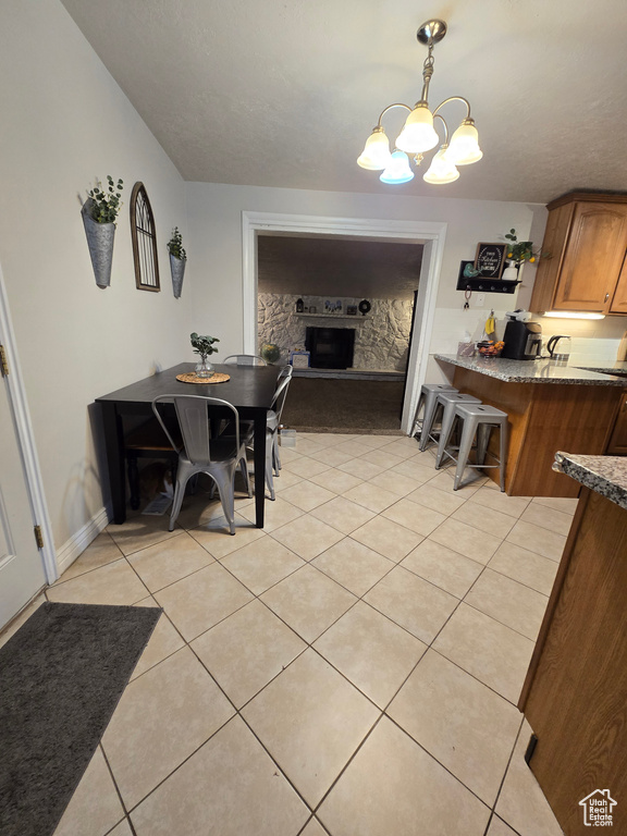 Dining area featuring a chandelier, light tile patterned floors, a fireplace with raised hearth, and baseboards