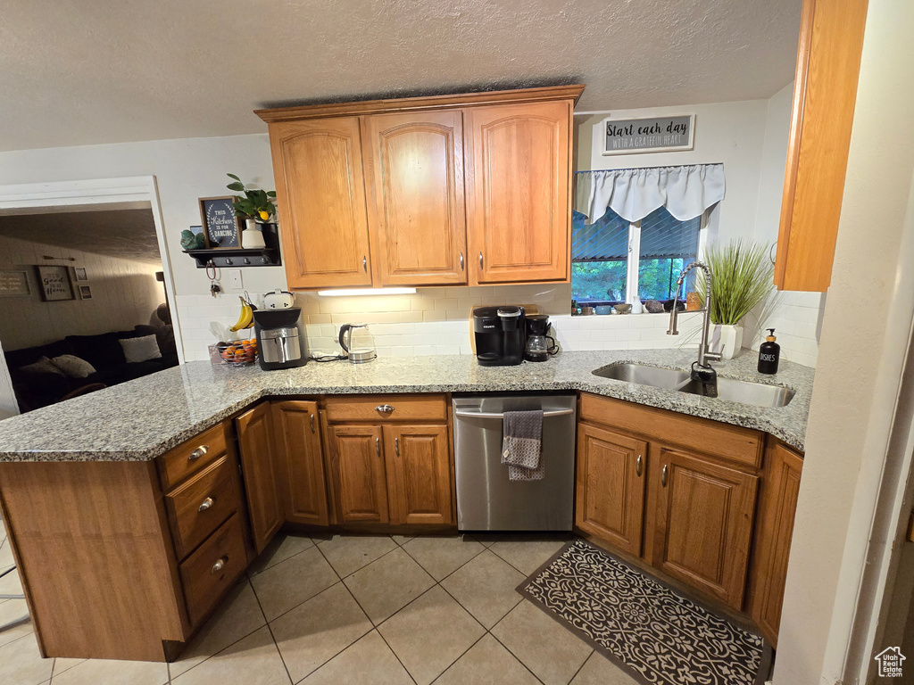 Kitchen featuring dishwasher, a sink, a peninsula, light tile patterned floors, and light stone counters