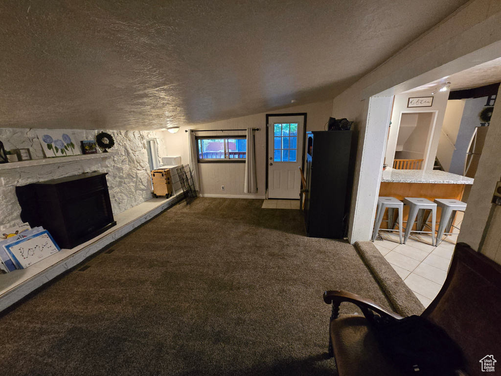 Carpeted living room with a textured ceiling, vaulted ceiling, a stone fireplace, and tile patterned floors