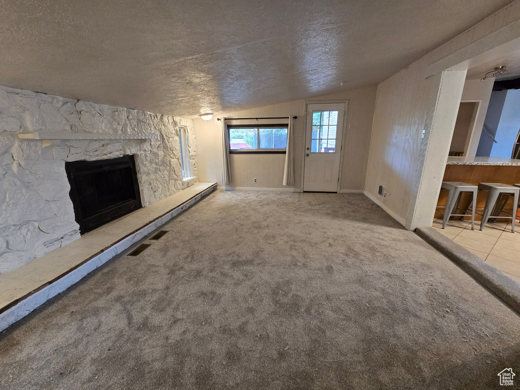 Unfurnished living room featuring lofted ceiling, a textured ceiling, a fireplace, and carpet flooring