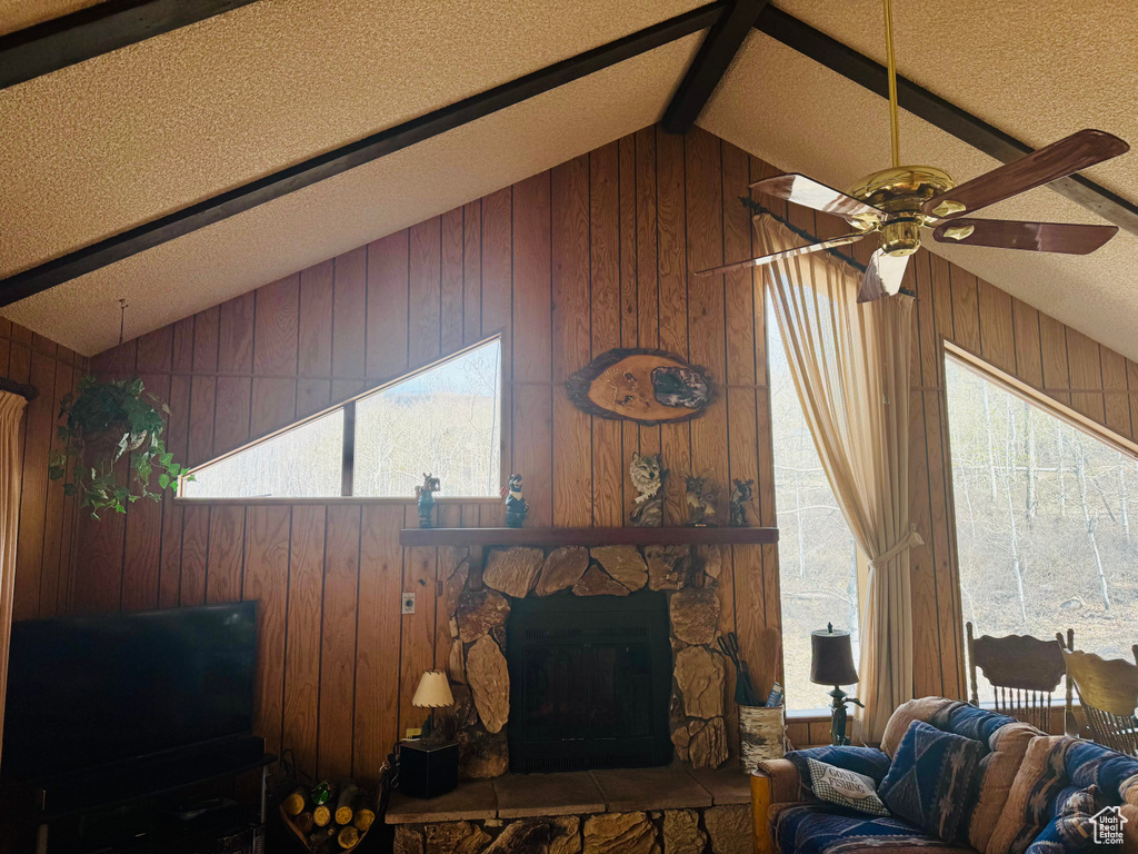 Living area featuring wooden walls, a ceiling fan, a fireplace, and a textured ceiling
