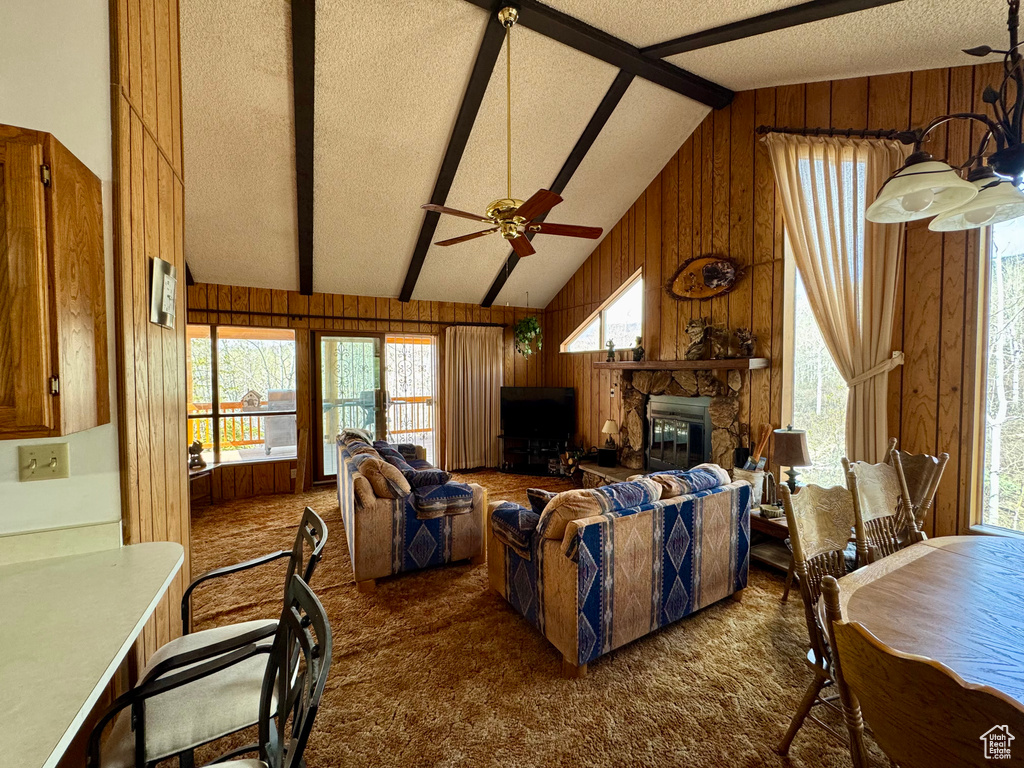 Living area with wood walls, dark carpet, a ceiling fan, a fireplace, and high vaulted ceiling