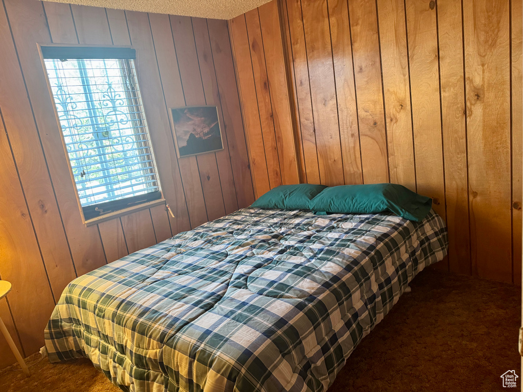 Bedroom with dark carpet, wood walls, and multiple windows