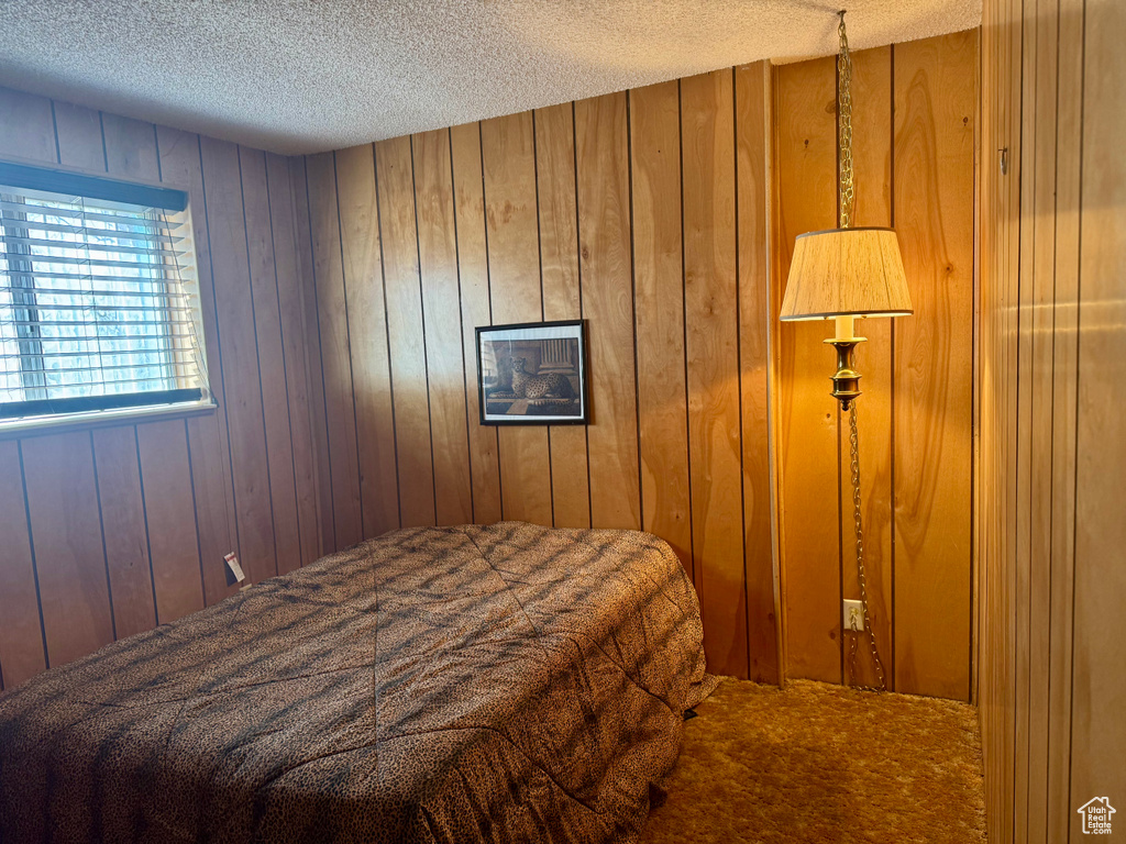 Bedroom featuring carpet flooring, a textured ceiling, and wooden walls