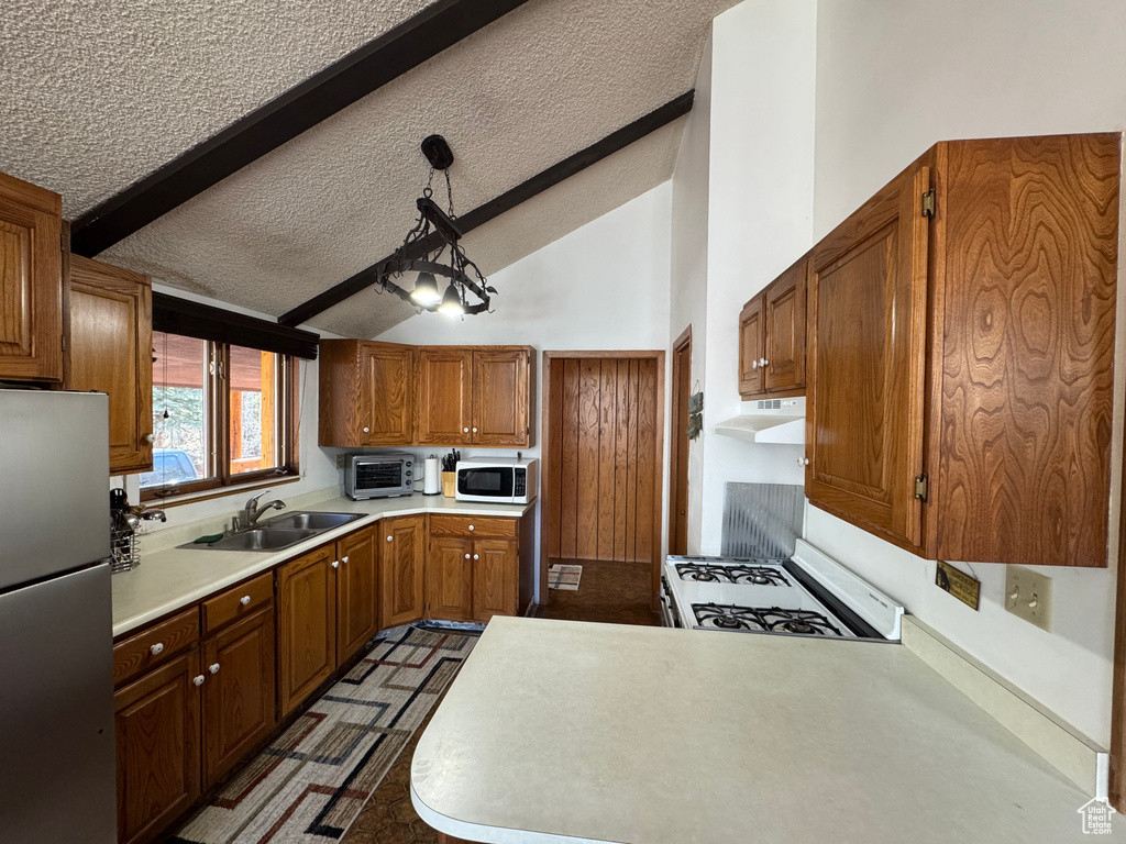Kitchen with white appliances, a sink, under cabinet range hood, light countertops, and a textured ceiling