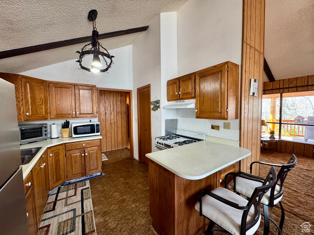 Kitchen featuring white appliances, a textured ceiling, under cabinet range hood, high vaulted ceiling, and light countertops