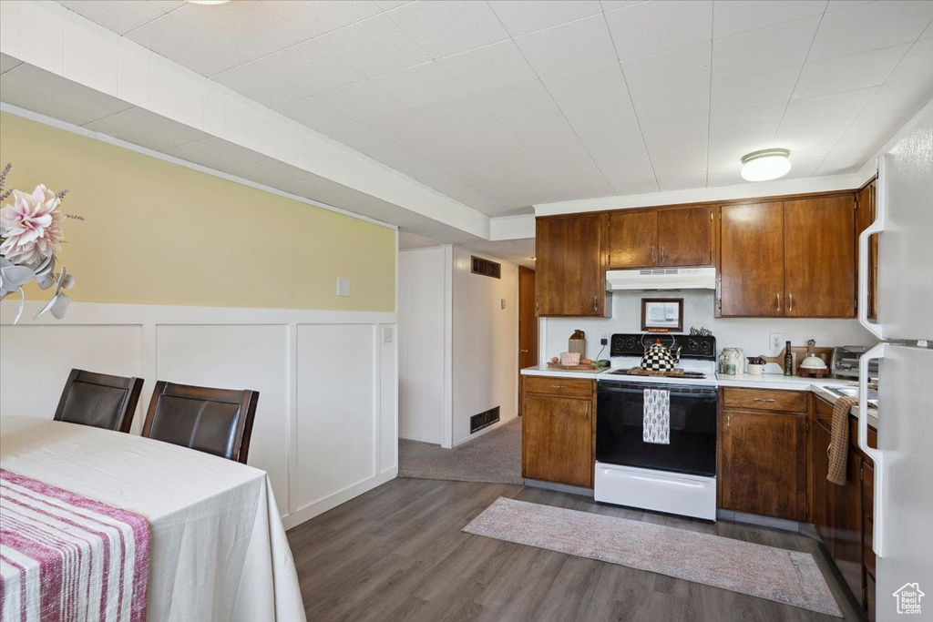 Kitchen featuring range with electric cooktop, light countertops, under cabinet range hood, dark wood finished floors, and brown cabinetry