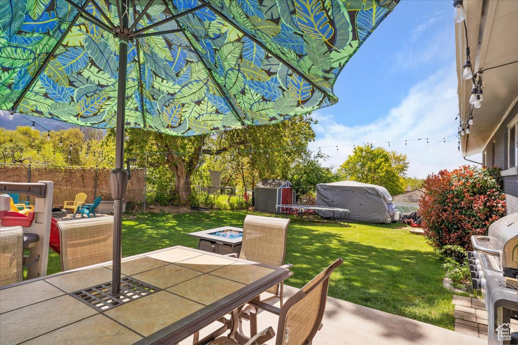 View of patio with outdoor dining area, a storage unit, an outdoor structure, and a fire pit