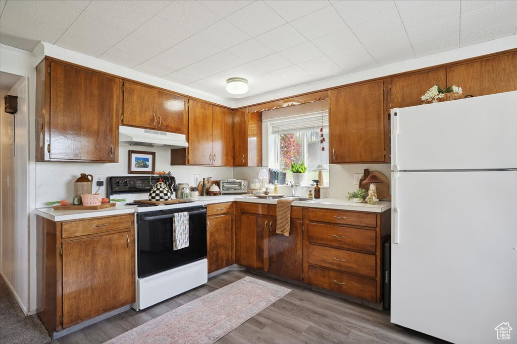 Kitchen featuring freestanding refrigerator, electric range, under cabinet range hood, light countertops, and brown cabinetry