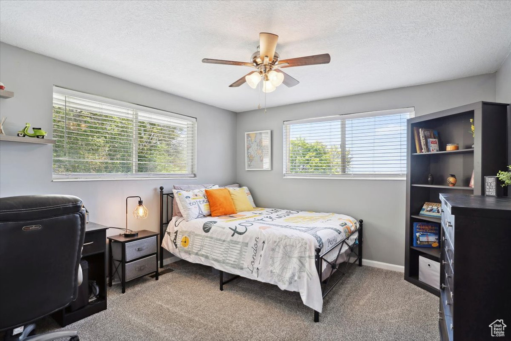 Bedroom with multiple windows, carpet flooring, a textured ceiling, a ceiling fan, and an office area