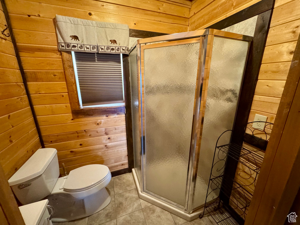 Bathroom featuring wooden walls, toilet, a stall shower, and tile patterned flooring