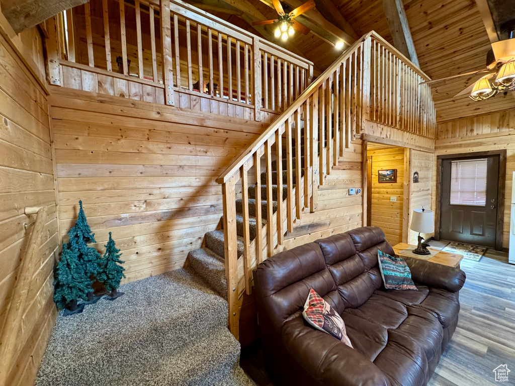 Living room featuring wood walls, wood finished floors, a ceiling fan, wooden ceiling, and stairway