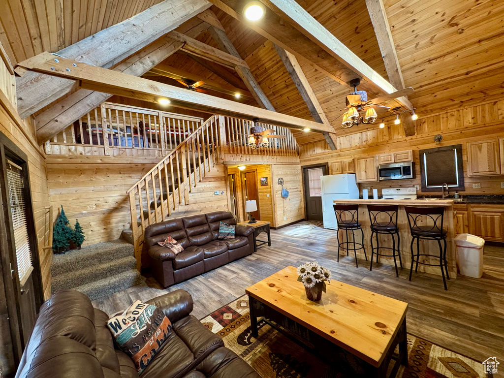 Living area featuring stairway, a chandelier, wooden walls, wood finished floors, and beamed ceiling
