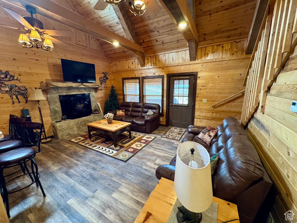 Living room featuring ceiling fan, wood walls, wood ceiling, wood finished floors, and a stone fireplace