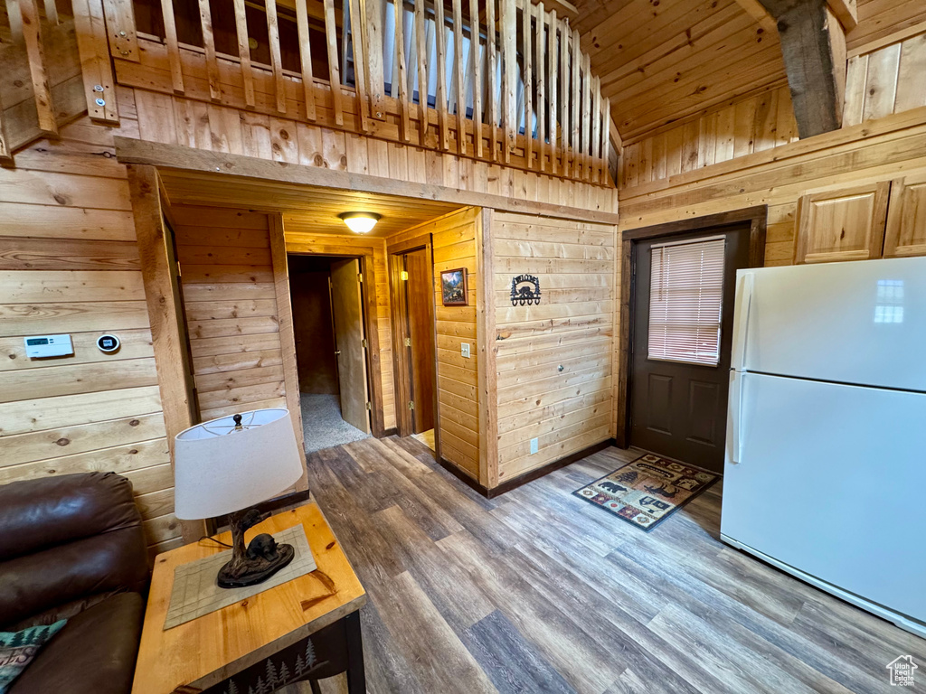 Kitchen with freestanding refrigerator, wooden walls, wood finished floors, and high vaulted ceiling