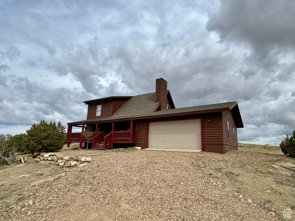 Rear view of house with log veneer siding, an attached garage, a chimney, a porch, and a shingled roof