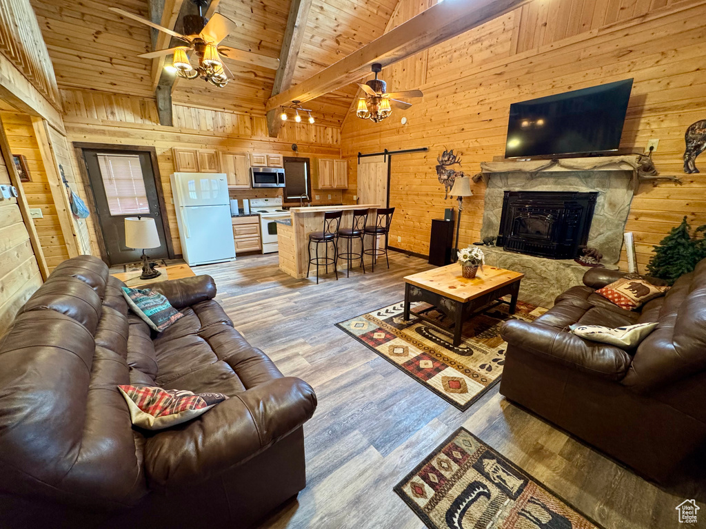 Living area with a ceiling fan, wooden walls, a barn door, beam ceiling, and wood finished floors