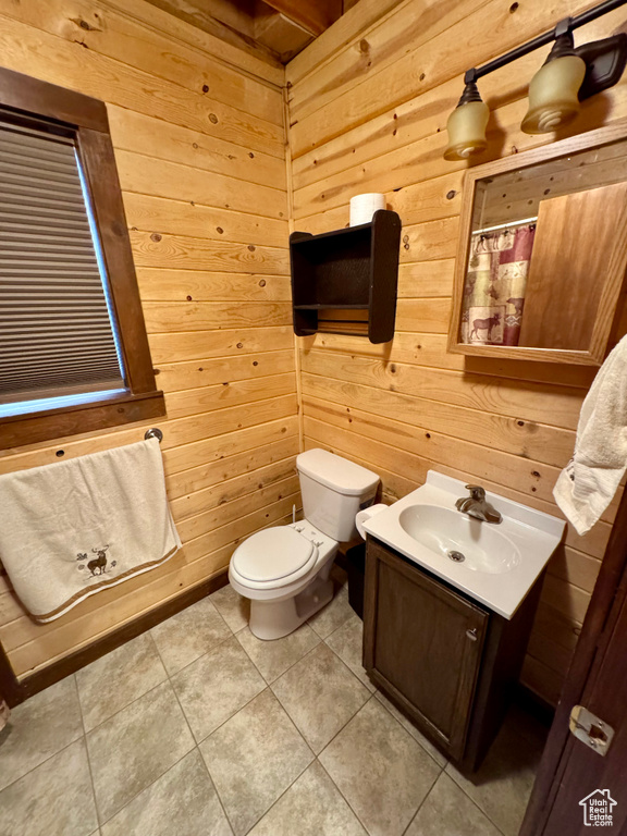 Bathroom featuring wood walls, toilet, vanity, tile patterned floors, and curtained shower