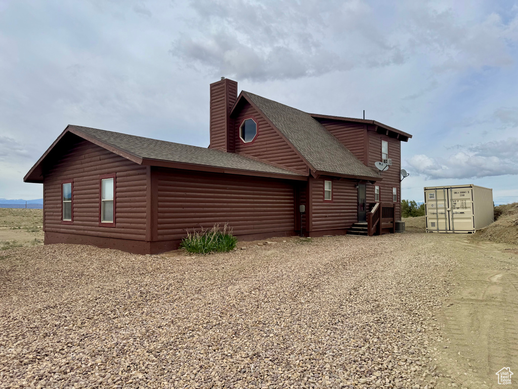 View of home\'s exterior featuring a shingled roof, a chimney, driveway, and log veneer siding