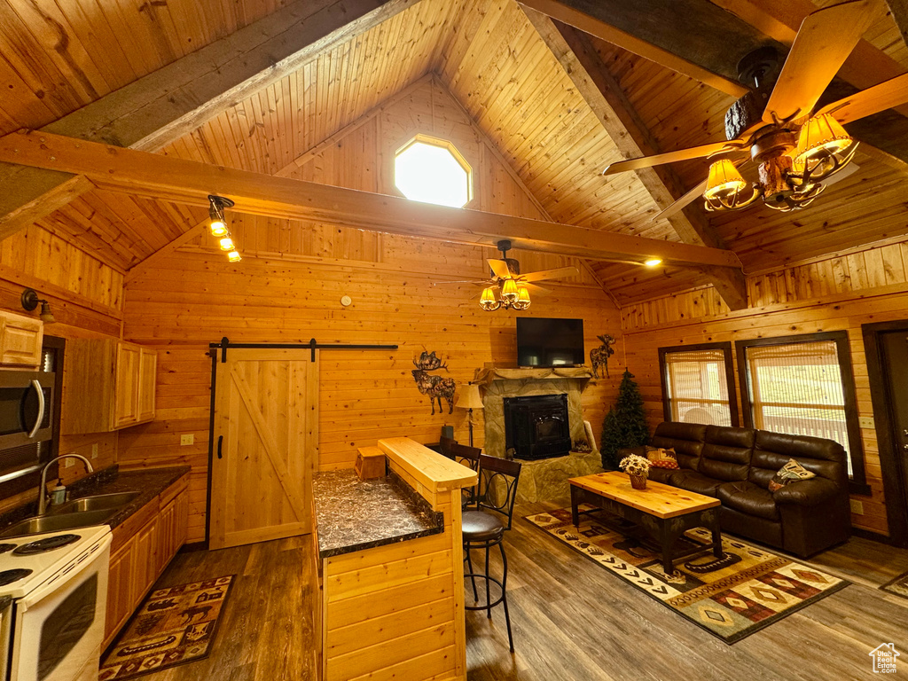 Living room featuring a barn door, ceiling fan, wooden ceiling, wooden walls, and a stone fireplace