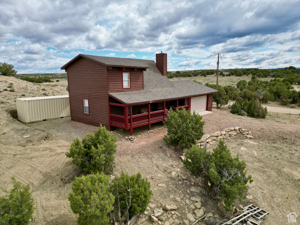 View of front of home featuring roof with shingles, an attached garage, dirt driveway, a chimney, and faux log siding