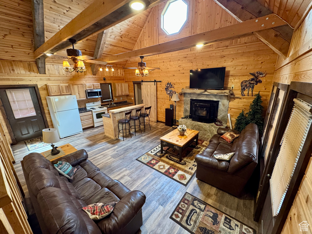 Living area featuring a stone fireplace, ceiling fan, wooden walls, high vaulted ceiling, and light wood-style floors