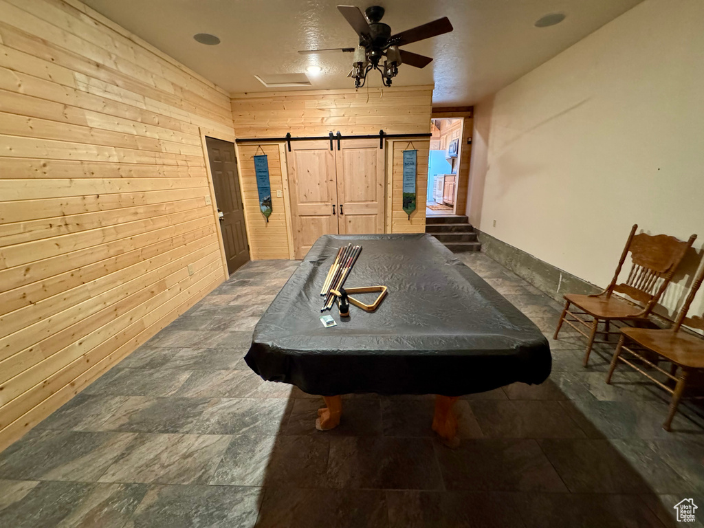 Rec room featuring wooden walls, a barn door, billiards, stone finish floors, and a ceiling fan